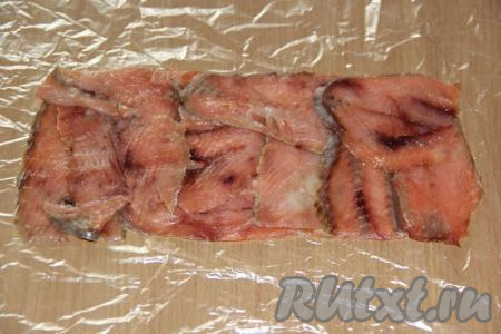 На пищевую плёнку выложить тонкие ломтики красной рыбы в прямоугольный пласт (как на фото).