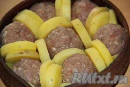 На дно круглой жаропрочной формы выложить кружочки картошки в один слой. Затем на слой картошки выложить фрикадельки, перекладывая их дольками картошки (как на фото).