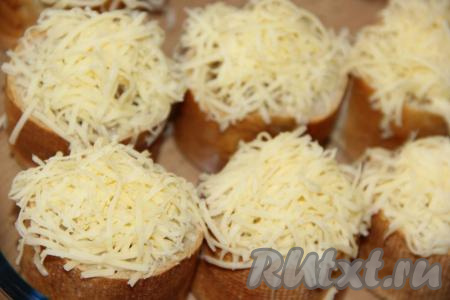 Сыр натереть на мелкой тёрке и пышной шапочкой выложить поверх грибной начинки. Переложить багет с начинкой на противень и поставить в разогретую духовку.