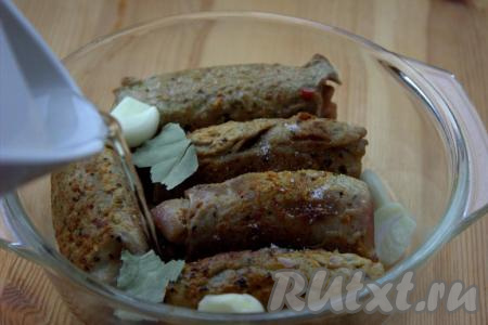 Обжаренные свиные рулетики с грибной начинкой выложить в жаропрочную форму. Добавить лавровый лист, очищенные и разрезанные пополам зубчики чеснока, влить воду (уровень воды должен доходить до половины высоты рулетиков), при необходимости, подсолить.