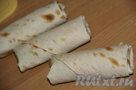 Края каждого квадрата из лаваша подвернуть с двух сторон, а потом свернуть рулетом. Получатся рулетики из лаваша с начинкой из сосисок, сыра и огурцов.