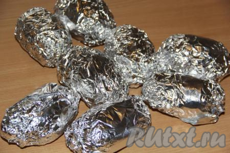 Плотно завернуть каждую картофелину в фольгу, выложить на противень и запекать в разогретой духовке, примерно, 45-55 минут при температуре 250 градусов. Время запекания зависит от размера картофеля (готовность можно проверить с помощью зубочистки - готовая картофелина будет легко прокалываться). 