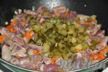 Перемешать сердечки с овощами, накрыть крышкой и потомить минут 10 на небольшом огне. Солёные огурцы, нарезанные на кубики среднего размера, выложить в сковороду к куриным сердечкам, влить 100 мл горячей воды, после закипания уменьшить огонь. Сковороду накрыть крышкой и тушить сердечки 10 минут.