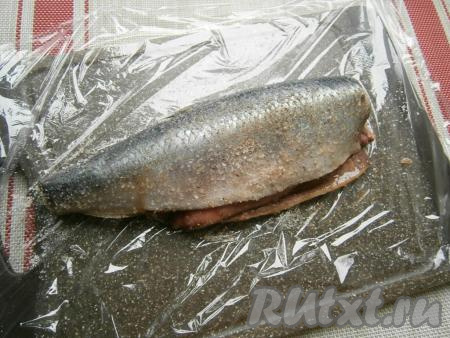 Селёдку поместить на пищевую плёнку и хорошенько натереть рыбку внутри и снаружи солью, смешанной со специями.