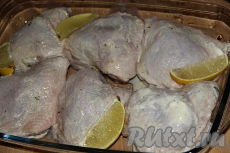Замаринованные кусочки курицы выложить в жаропрочную форму.  Оставшийся маринад не нужно выливать в форму. Не использованную половинку лимона нарезать на дольки и выложить в форму поверх курицы.