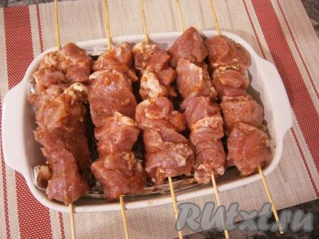 Миску накрыть крышкой и оставить мясо с помидорами и луком в прохладном месте на 4-5 часов, а лучше - на всю ночь. Деревянные шпажки предварительно замочить в горячей воде на 10-15 минут (чтобы не горели в духовке) и нанизать на них замаринованную в томате свинину. Шпажки расположить на прямоугольной форме для запекания, в которую налить воду (на 1/3 объема).