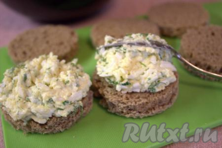 На подсушенные и остывшие кружочки хлеба выложить по 1-2 чайных ложки подготовленной начинки из яиц, сыра, чеснока и зелени.