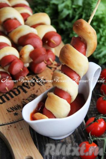 Аппетитные, вкусные, сытные сосиски в тесте, запечённые в духовке, можно подать, не снимая шпажки, в горячем виде с любимым соусом (например, они отлично сочетаются с кетчупом). 