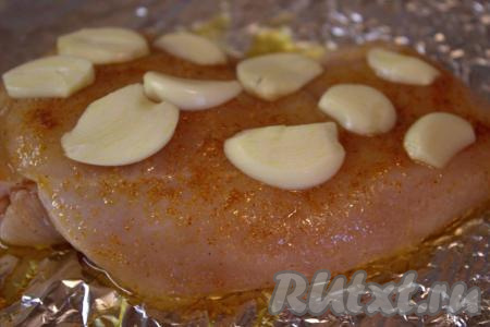 Куриное филе посолить, хорошо смазать получившимся ароматным маслом (если время позволяет, филе можно оставить промариноваться минут на 20). На край листа фольги выложить куриное филе, разложить поверх мяса пластины чеснока.