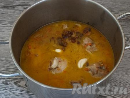 Залейте 1,5 стаканами воды, закройте крышкой, дайте закипеть, а затем варите на среднем огне 1 час. По истечении времени добавьте изюм и неочищенный чеснок, снова закройте крышкой и варите ещё 30 минут.