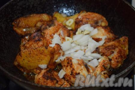 В сковороду с куриным мясом добавляем нарезанные лук и чеснок, обжариваем овощи на среднем огне в течение 4-5 минут.