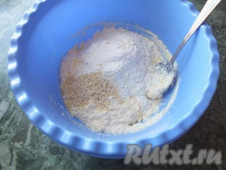 Добавьте к творожно-масляной массе разрыхлитель для теста, 2 чайные ложки кунжута, часть муки, перемешайте ложкой.