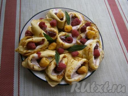 Наполнить блинчики 1-2 столовыми ложками смеси из сметаны и варенья, сверху выложить свежую малину. Украсить блюдо листиками мяты.