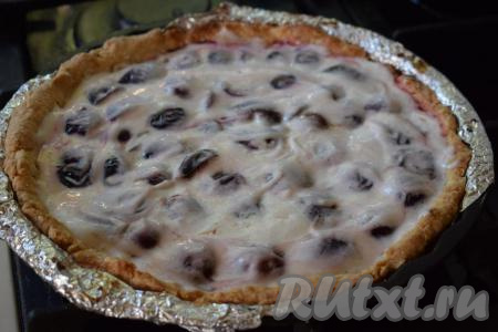 Достаём песочный пирог из духовки, покрываем сливы сметанной заливкой, аккуратно распределяя её ложкой по всей поверхности пирога.
