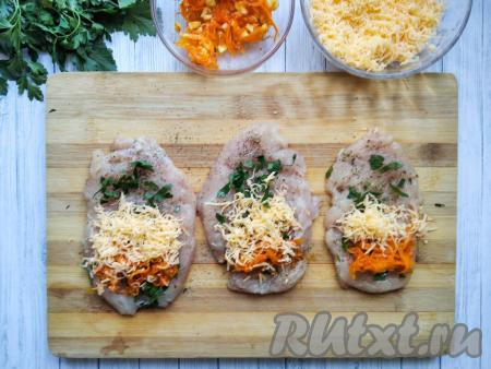 На каждый отбитый кусочек куриного филе выложить часть измельчённой петрушки, часть остывшей моркови, обжаренной с чесноком, и посыпать частью натёртого сыра.