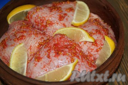 Выложить замаринованные части курицы в жаропрочную форму. Вторую половину лимона нарезать на дольки и выложить на кусочки курочки.