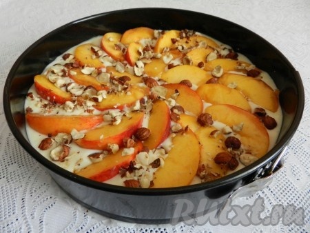 Сверху разложить дольки персиков и посыпать орехами. Поставить персиковый пирог в духовку на 45-50 минут при 170 градусах.