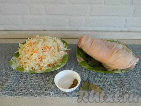 В первую очередь займёмся подготовкой продуктов. Свиную рульку моем, зачищаем ножом кожу и обсушиваем. 500 грамм квашеной капусты (у меня собственного приготовления, но подойдёт и магазинная) перекладываем в большую тарелку. Очищаем 3 зубчика чеснока и 1 луковицу.