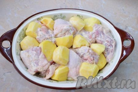 В подготовленную форму для запекания выложите куриные бёдра и распределите между ними картофель. Крупный картофель можно разрезать на 2-3 части - так он быстрее приготовится. Остатки сметанного маринада размажьте сверху по картофелю.