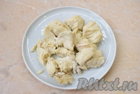 Чтобы куриное мясо быстрее остыло, извлеките его из бульона и поломайте на кусочки. После остывания мясо мелко нарежьте.