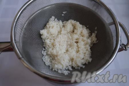 К этому времени рис уже дошёл до состояния полуготовности. Откидываем его на дуршлаг и промываем под холодной проточной водой, даём стечь лишней жидкости.