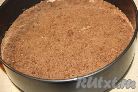 Разделить массу на две части (та часть, которая будет нижним коржом, должна быть немного больше). В форму для выпечки (у меня разъёмная форма диаметром 25 см) выложить часть крошки, предназначенную для нижнего коржа (эта часть крошки немного больше оставшейся), и утрамбовать. Поставить на 30 минут в холодильник. 