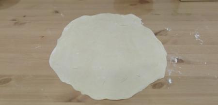 Посыпаем стол мукой и начинаем скалкой раскатывать одну часть теста. Тесто равномерно раскатываем от середины к краям. Стараемся раскатывать очень тонко, до полупрозрачного состояния. Можно даже помогать руками, растягивая тесто. Получается достаточно большая и тонкая лепёшка.