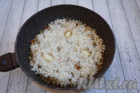 За время тушения свинины вода практически вся выпарилась. К овощам и мясу добавляем рис. Делаем 3 углубления в рисе до самого дна сковороды и вставляем туда 3 очищенных зубчика чеснока.