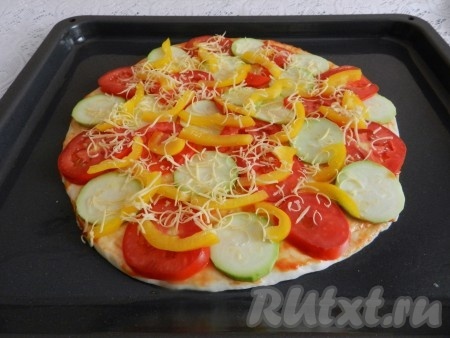 Сыр натереть на крупной тёрке и присыпать им сверху пиццу.  Поставить пиццу с начинкой из кабачков, помидоров и перца в разогретую до 220 градусов духовку на 15-20 минут.
