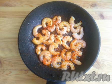 Зубчики чеснока пропустить через пресс (или натереть на средней тёрке). Перевернуть  креветки, выложить подготовленный чеснок, добавить специи по вкусу. Продолжать готовить около 1-2 минут. Недожаренные креветки имеют вытянутую форму, пережаренные экземпляры сворачиваются в кружок. Идеально жареная креветка должна быть, как буква «С». Общее время термообработки морепродуктов не должно превышать 5 минут.