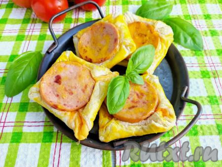 Готовые слойки с колбасой и сыром переложить на тарелку для подачи, дать немного остыть, украсить свежей зеленью и подать к столу. Слойки получаются сытными, с хрустящей основой и колбасно-сырным вкусом.