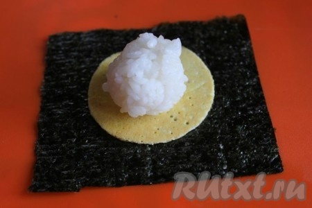 На квадратный лист нори на его матовую сторону уложите яичный блинчик и на него порцию риса.