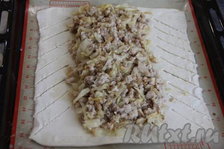 Жарить капусту с фаршем минут 15, разбивая комочки мяса. Затем посолить, добавить пропущенный через пресс чеснок, перемешать и потомить на небольшом огне ещё минут 5. Снять с огня, дать остыть и начинка из капусты и фарша для пирога готова. Размороженное слоёное тесто на присыпанной мукой поверхности раскатать скалкой в прямоугольный пласт (я раскатала в пласт размером, примерно, 28 на 24 сантиметра). Противень застелить тефлоновым ковриком (или пергаментом), затем переложить раскатанное тесто. В центр раскатанного теста в длину выложить остывшую начинку из капусты и фарша. Края теста с двух длинных сторон разрезать на полоски шириной примерно 2 сантиметра, как на фото.