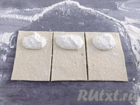 Рабочую поверхность  присыпаем мукой, тесто делим на две части, чтобы с ним было удобно работать. Одну часть теста раскатываем скалкой в тонкий пласт, срезаем неровные края и нарезаем на прямоугольники размером 10 на 15 сантиметров. Работать с этим творожным тестом очень удобно. На каждый прямоугольник теста с узкой стороны, отступив немного от краёв, выкладываем примерно одну столовую ложку начинки и сворачиваем в рулетик, начиная со стороны с начинкой.