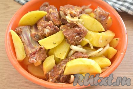 Выкладываем к картошке и луку замаринованные свиные рёбрышки и лавровые листья, тщательно перемешиваем.