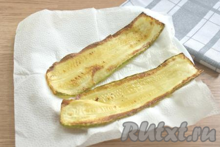 Разогреваем на сковороде растительное масло. Стряхиваем с полосок кабачка лишнюю муку, а затем выкладываем их на сковороду в разогретое масло в один слой. Обжариваем кабачки до подрумянивания с двух сторон (ориентировочно минуты по 2-3 с каждой стороны). Обжаренные полоски кабачков выкладываем на бумажные салфетки (или бумажные полотенца), чтобы удалить лишнее масло. Постепенно покрываем мукой и обжариваем все полоски из кабачка. Даём им немного остыть.
