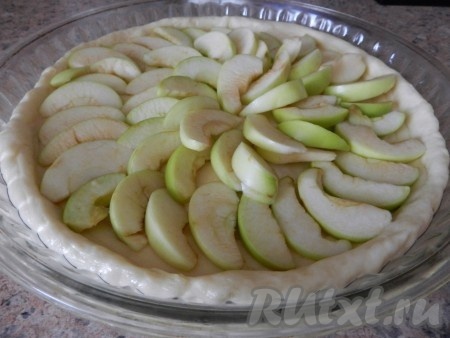 На тесто выложить нарезанные дольками яблоки, присыпать сахаром.