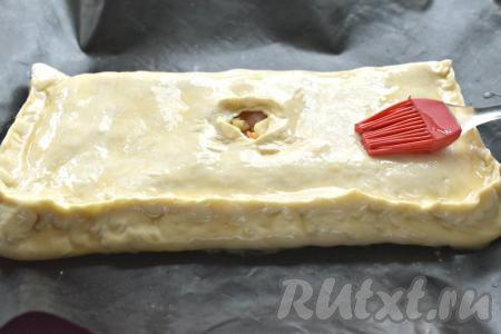 Накрываем начинку второй стороной пласта, плотно скрепляем края, а в центре оформляем отверстие для выхода пара. Взбиваем слегка яйцо, а затем получившейся яичной смесью смазываем поверхность слоёного пирога.