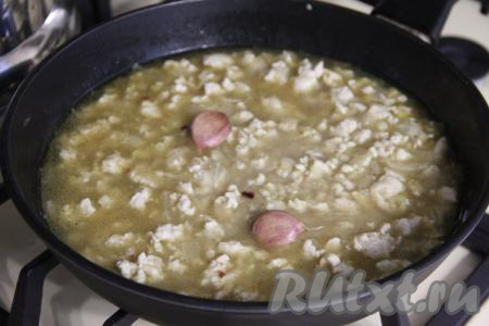 Влить сковороду с рисом и куриным фаршем 400 миллилитров горячей воды, перемешать. Зубчик чеснока промыть водой, убрать с него загрязнения и, не очищая, разрезать пополам, выложить на поверхность риса.