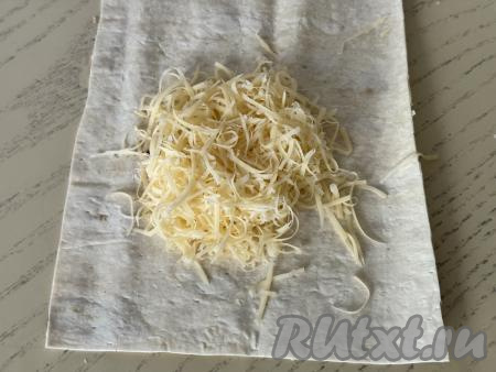 На каждый прямоугольник из лаваша чуть ближе к одной короткой стороне лаваша выложить примерно 2 столовых ложки натёртого сыра 