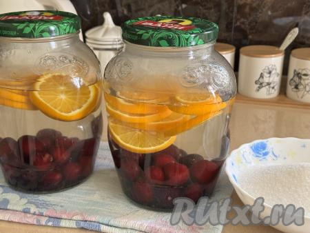 Вскипятить 2 литра воды. В каждую банку с черешней и апельсином влить 1 литр кипящей воды, прикрыть банки прокипячёнными крышками, оставить на 20 минут. 
