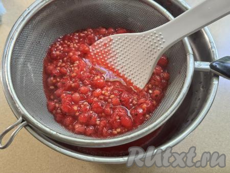 Взять миску, поверх неё поставить сито. Откинуть проваренную ягодную массу на сито и с помощью лопатки (или столовой ложки) перетереть смородину через сито в миску. В результате в миске будет пюре без косточек из красной смородины, а сите останется практически сухой жмых с косточками (этот жмых нам не понадобится). 