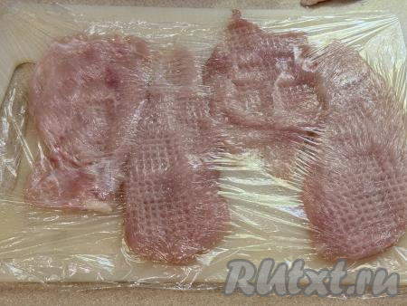 Выложить кусочки куриного мяса на разделочную доску, накрыть пищевой плёнкой. Отбить куриное филе с помощью кухонного молоточка до толщины 5-7 миллиметров. 