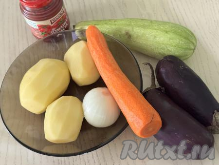 Подготовить продукты для приготовления картошки, тушёной с кабачками и баклажанами. Картошку, морковь и лук почистить. Картошку выложить в миску, залить полностью холодной водой, чтобы картофель не потемнел, пока мы будем заниматься другими овощами. Баклажаны вымыть. Кабачок я взяла с тонкой кожицей и мелкими семечками, поэтому просто обрезала у него кончики с двух сторон и промыла водой. Если у кабачка жёсткая кожура - её нужно будет срезать, крупные семечки нужно будет удалить. 