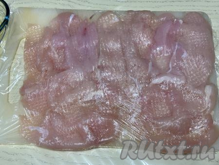 Выложить кусочки мяса на разделочную доску в один слой, накрыть филе пищевой плёнкой и слегка отбить кулинарным молоточком. 