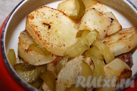Обжаренный картофель выложить в горшочек к мясу, добавив нарезанный соленый огурец.