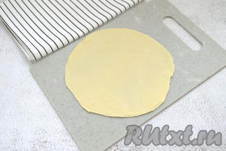 На слегка присыпанной мукой поверхности вначале одну часть теста раскатываем в тонкую лепёшку толщиной 2 миллиметра, ориентировочно диаметром 16 сантиметров. Края лепёшки я подравняла, приложив сверху тарелку диаметром 16 сантиметров и отрезав лишнее тесто.