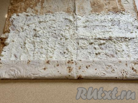 Свернуть лаваш с творогом в плоский рулет, начиная с более узкой стороны. 