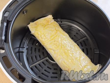 Яичный желток в небольшой ёмкости взбить вилкой до однородности. Вначале одну часть рулета с творогом выложить в чашу аэрогриля, смазать поверхность лаваша взбитым желтком. 