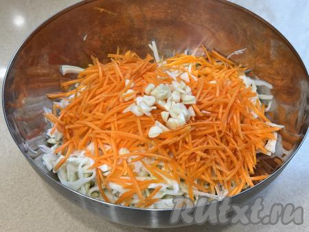 В миску с капустой добавить морковку, натёртую на крупной тёрке, и нарезанный на достаточно тонкие пластинки чеснок. 